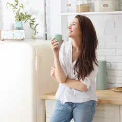 Kobieta z kubkiem w kuchni, zastanawia się, czy koenzym q10 rano czy wieczorem będzie lepszy.