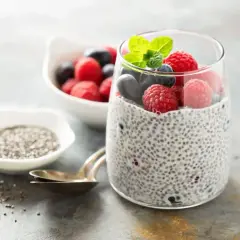 Pudding chia z owocami leśnymi, pokazujący jak przygotować nasiona chia. Obok miseczka z nasionami i łyżeczki.