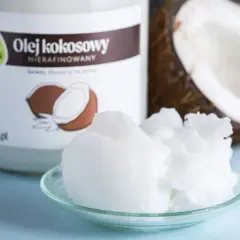 Olej kokosowy nierafinowany na talerzyku, idealny jako jaki olej do smażenia. Obok słoik i połówka kokosa.