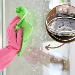 Rękawica w różowej gumie czyści szybę zieloną ściereczką. W okręgu widać miseczkę z wodą z octem, która jest naturalnym środkiem czyszczącym.