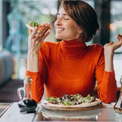 Kobieta w pomarańczowym golfie delektuje się pizzą, czując przypływ seratoniny.