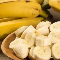 Kawałki bananów na drewnianej misce, obok całe banany. Czy banany a zakrzepica to dobry duet?