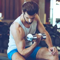 Mężczyzna ćwiczy biceps z hantlem w siłowni, skupiony na treningu.