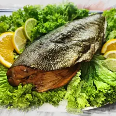 A whole trewal wędzony, presented on a bed of crisp lettuce, garnished with slices of orange and lime.