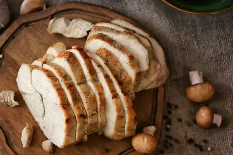 Pokrojona pierś z indyka na desce, obok czosnek i pieczarki. Zdrowe danie, które pozwoli Ci kontrolować pierś z indyka kcal.