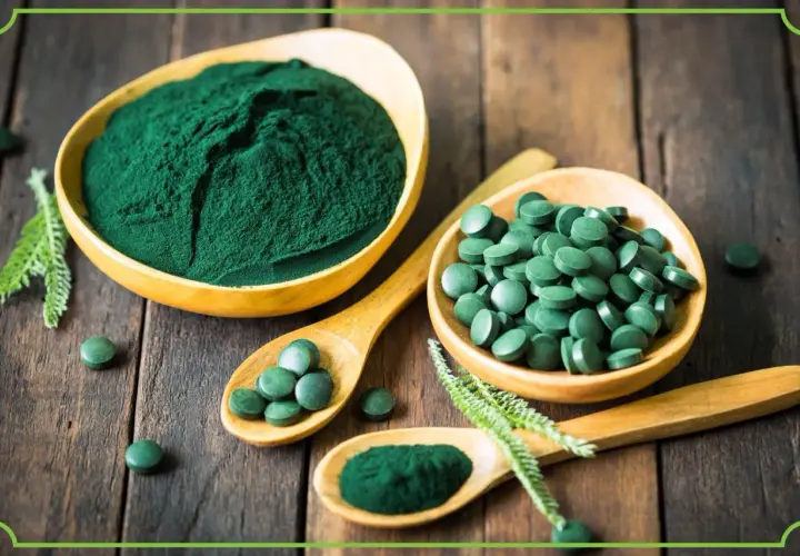 Zielona spirulina w proszku i tabletkach na drewnianym tle. Dowiedz się, spirulina co to jest i jakie ma właściwości.