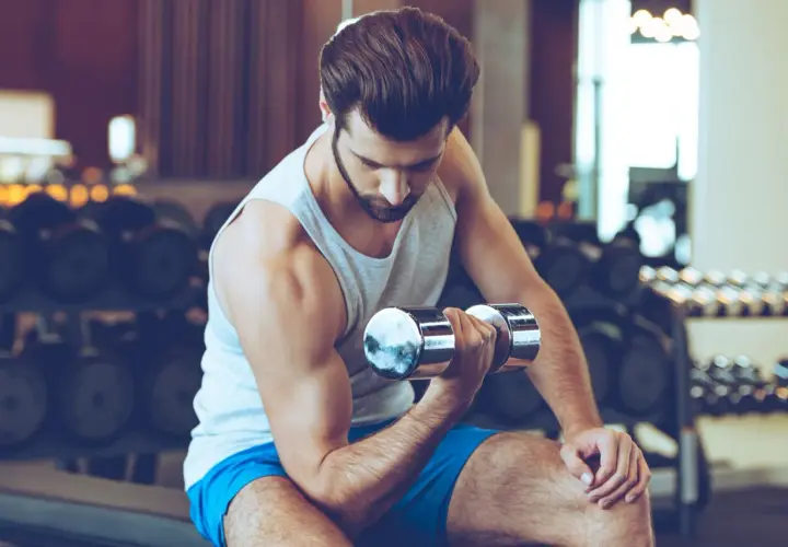 Mężczyzna ćwiczy biceps z hantlem w siłowni, skupiony na treningu.