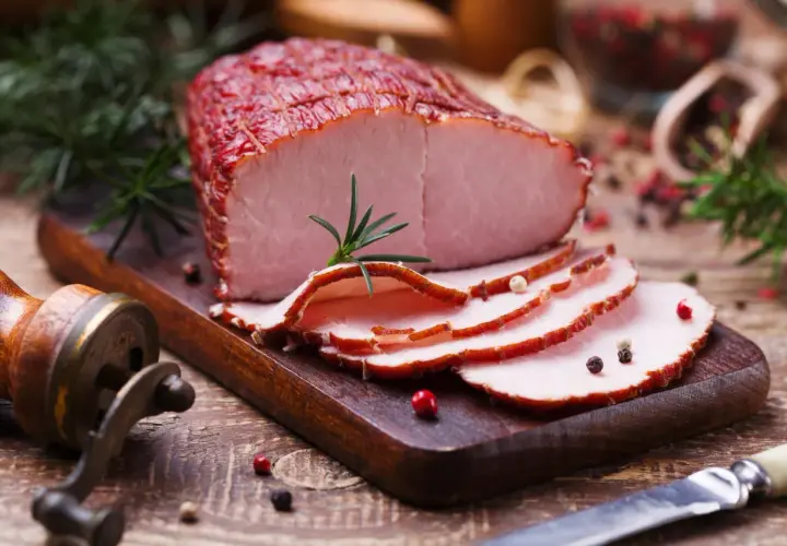 Pokrojona szynka wieprzowa na desce, ozdobiona rozmarynem i pieprzem. Idealna na kanapki, z niską zawartością szynka wieprzowa kcal.
