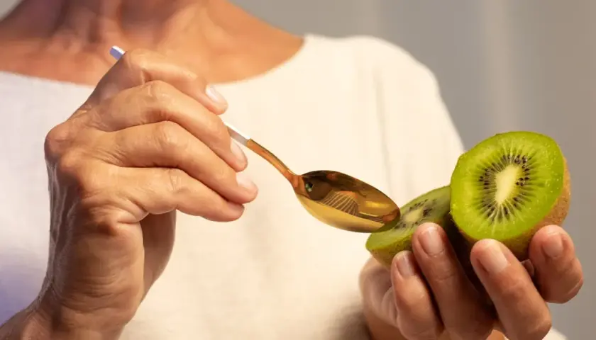 Dłoń trzyma połówkę kiwi, a złotą łyżeczką zbliża się do owocu, by poznać jego właściwości.