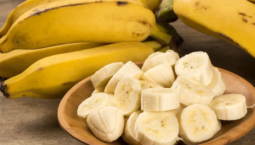 Kawałki bananów na drewnianej misce, obok całe banany. Czy banany a zakrzepica to dobry duet?