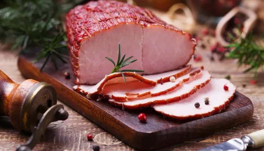 Pokrojona szynka wieprzowa na desce, ozdobiona rozmarynem i pieprzem. Idealna na kanapki, z niską zawartością szynka wieprzowa kcal.