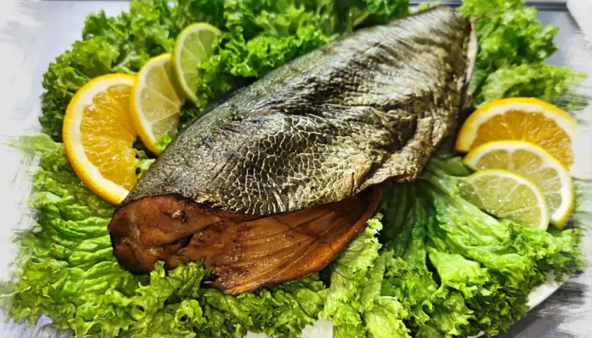 A whole trewal wędzony, presented on a bed of crisp lettuce, garnished with slices of orange and lime.