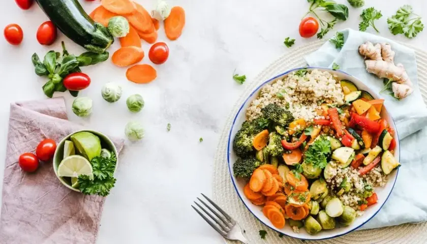 Kolorowa miska pełna warzyw i kaszy, idealna na dietę 1500 kcal. Obok świeże warzywa i limonka.