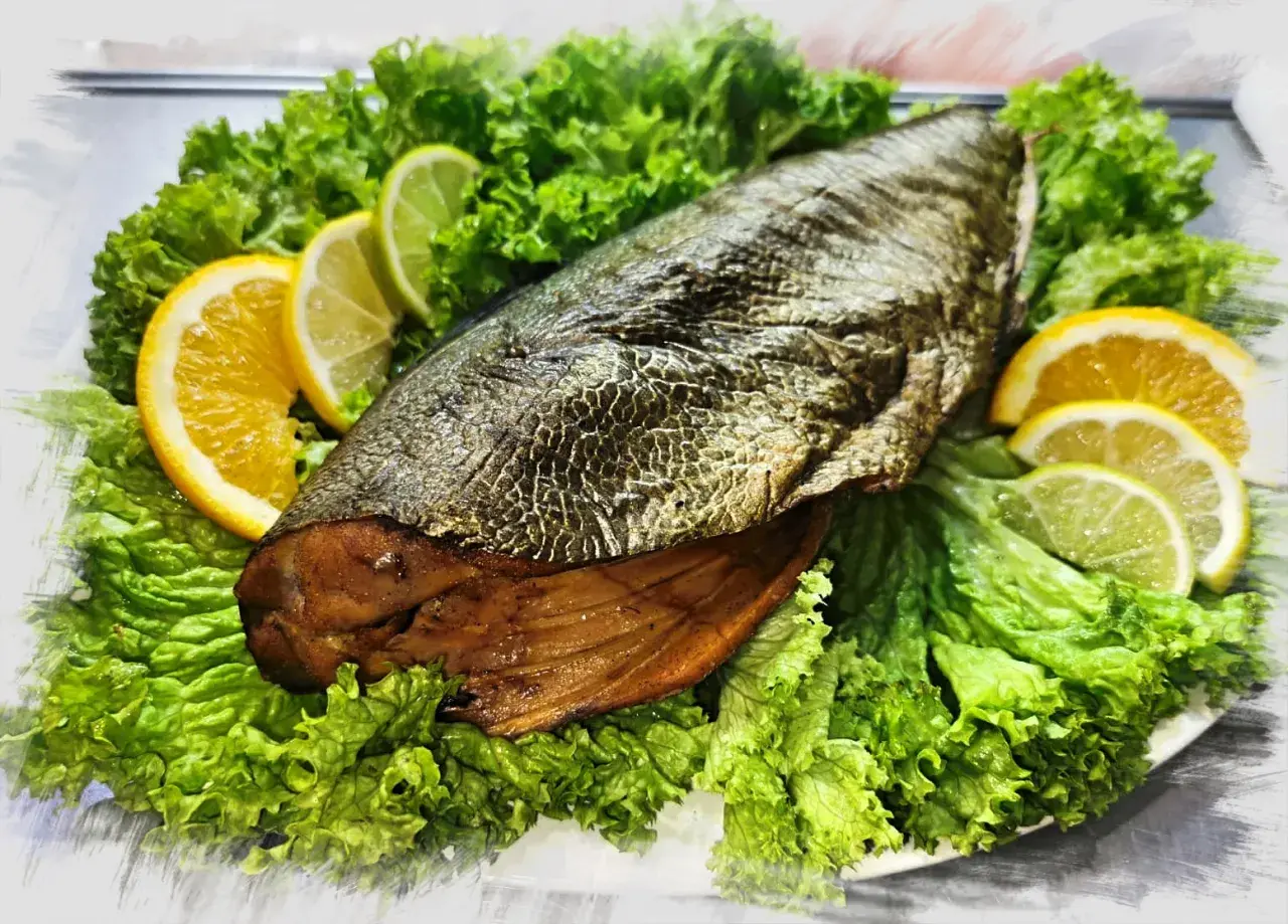A whole trewal wędzony, presented on a bed of crisp lettuce, garnished with slices of orange and lime.