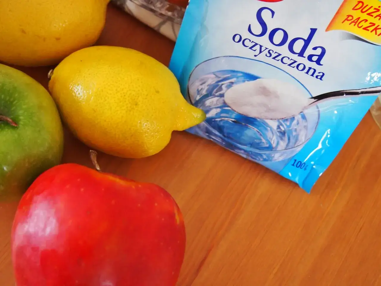 Opakowanie sody oczyszczonej obok jabłek i cytryn. Soda oczyszczona ma właściwości bakteriobójcze, co czyni ją wszechstronnym środkiem czystości.