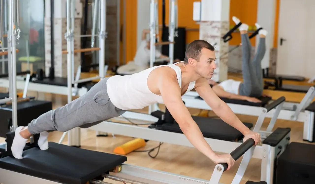 Mężczyzna na reformerze pilates w pozycji deski. Ćwiczenia te pomagają wzmocnić ciało i mogą przyczynić się do tego, czy pilates odchudza.
