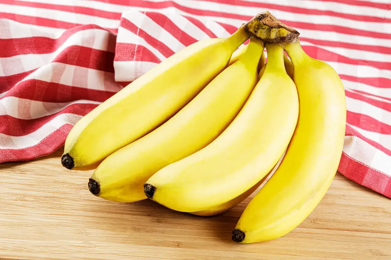 Pęczek żółtych bananów na drewnianej desce, obok czerwono-białej serwetki. Czy banany a zakrzepica to temat do rozważenia?