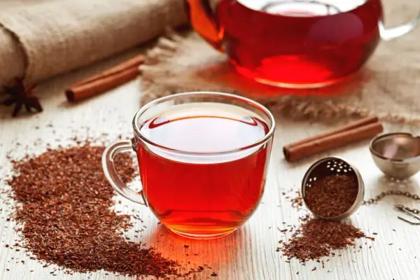 Aromatic rooibos właściwości: napar w szklance, susz, laska cynamonu i zaparzacz na drewnianym blacie.